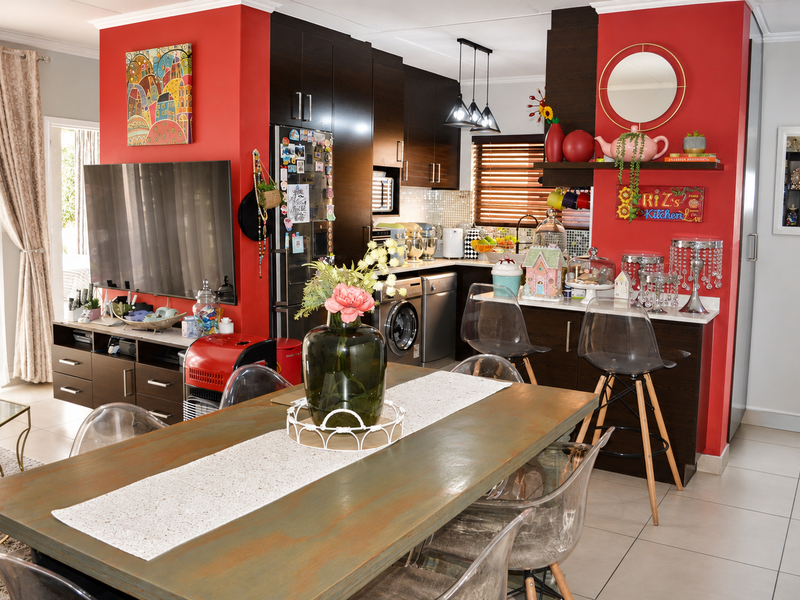An open-plan living and kitchen area featuring dark wood cabinetry, stone countertops, mosaic backsplash, and modern pendant lighting with ceramic floor tiles throughout.