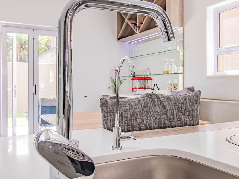 Modern kitchen featuring a sleek quartz countertop, stainless steel sink with chrome mixer tap, and integrated glass shelving with a built-in wine rack.