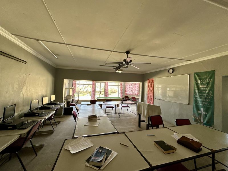 A large, multi-purpose utility or classroom space featuring a ceiling fan, whiteboard, and large windows, currently used for educational or group activities.