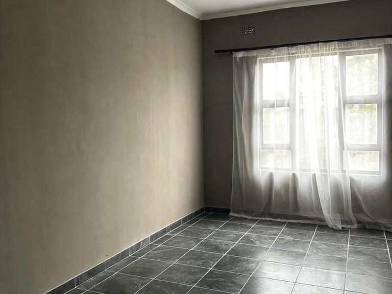An empty bedroom featuring dark tiled flooring, neutral walls, and a window with a curtain rod, offering a blank canvas for interior design.