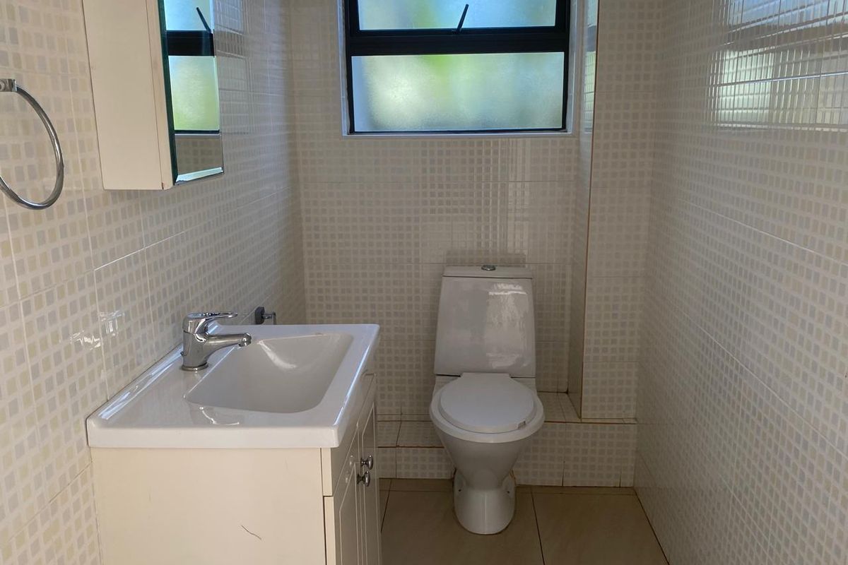A compact bathroom featuring a white vanity with integrated basin, a modern toilet, and fully tiled walls with a frosted window.