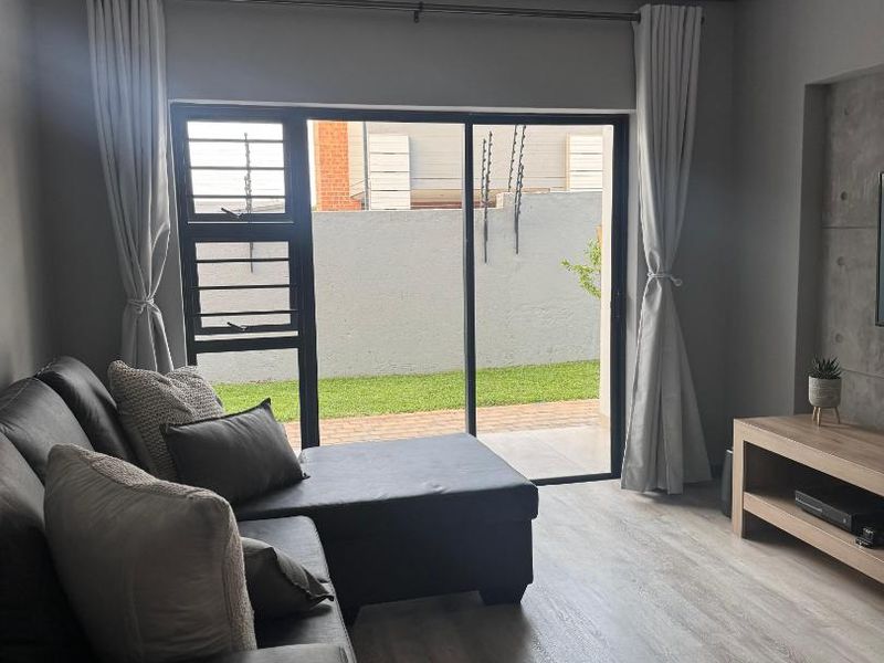 A modern living room featuring light laminate flooring, a concrete feature wall, and a large sliding glass door providing access to the rear garden.
