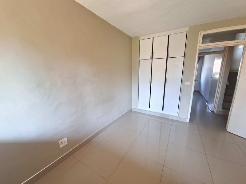 A vacant bedroom featuring neutral tiled flooring and white built-in cupboards, offering a clean and blank canvas for personalization.
