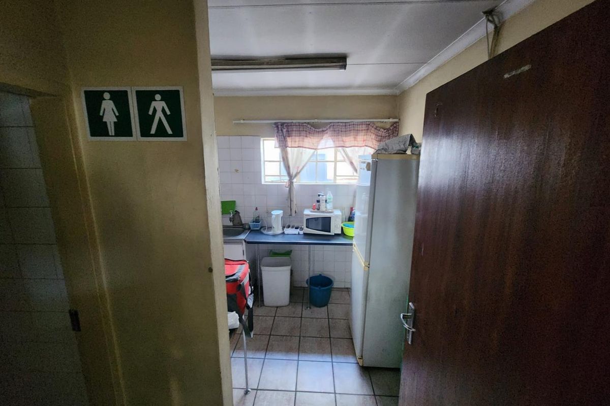 A compact kitchenette area featuring tiled flooring, basic cabinetry, and a sink, accessible via a doorway with signage.