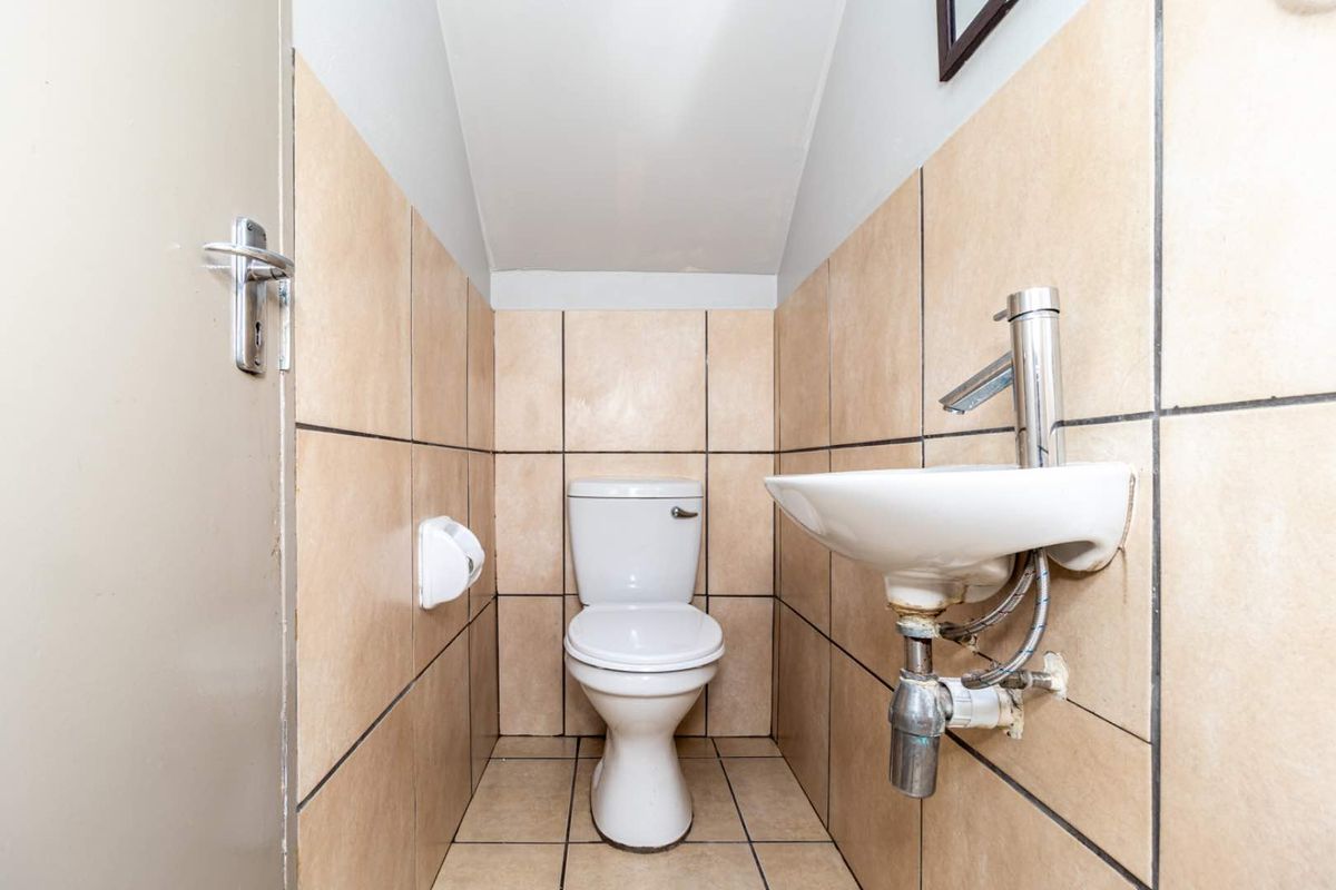 A compact guest cloakroom featuring a wall-mounted basin and a standard toilet, finished with neutral ceramic wall and floor tiles.
