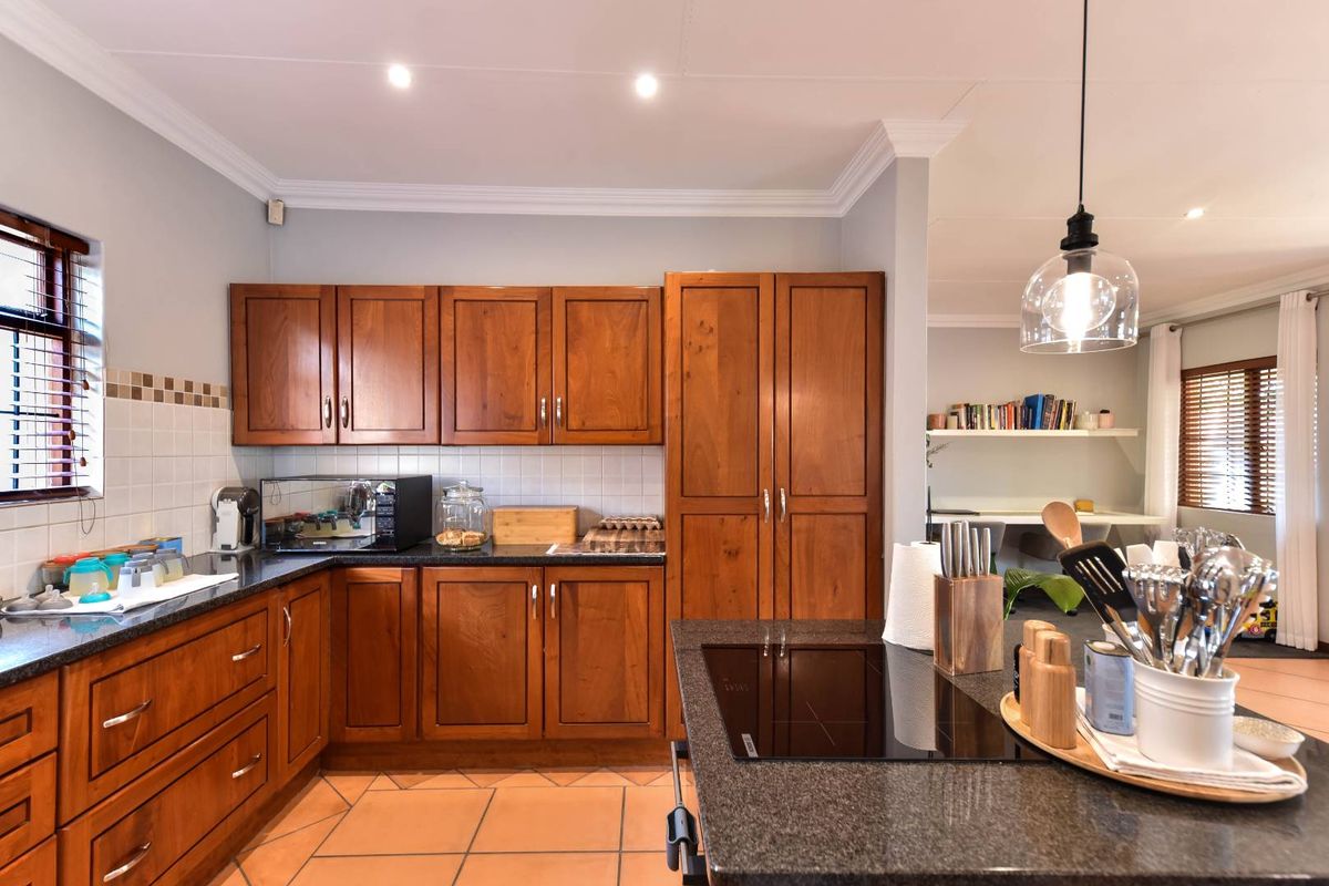 A well-maintained kitchen featuring warm wooden cabinetry, granite countertops, a built-in induction hob, and classic ceramic tile flooring with integrated lighting.