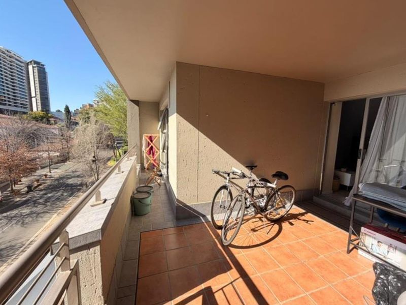 A covered balcony featuring tiled flooring and a metal balustrade, offering an elevated view of the surrounding urban area.