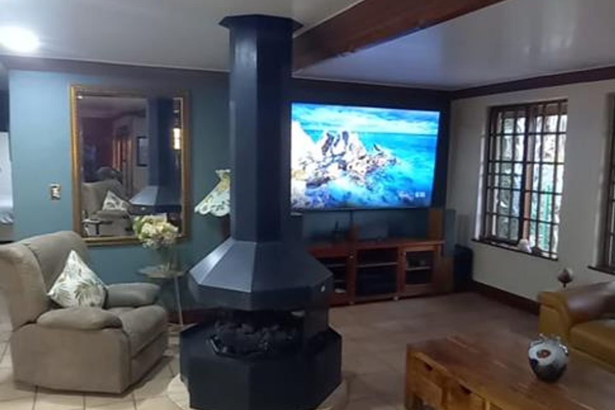 Spacious living room featuring a central freestanding fireplace, tiled flooring with decorative border, and exposed timber ceiling beams.
