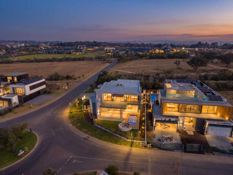 Aerial view of modern residential properties at dusk, featuring swimming pools, solar panels, and landscaped outdoor areas in a suburban estate setting.