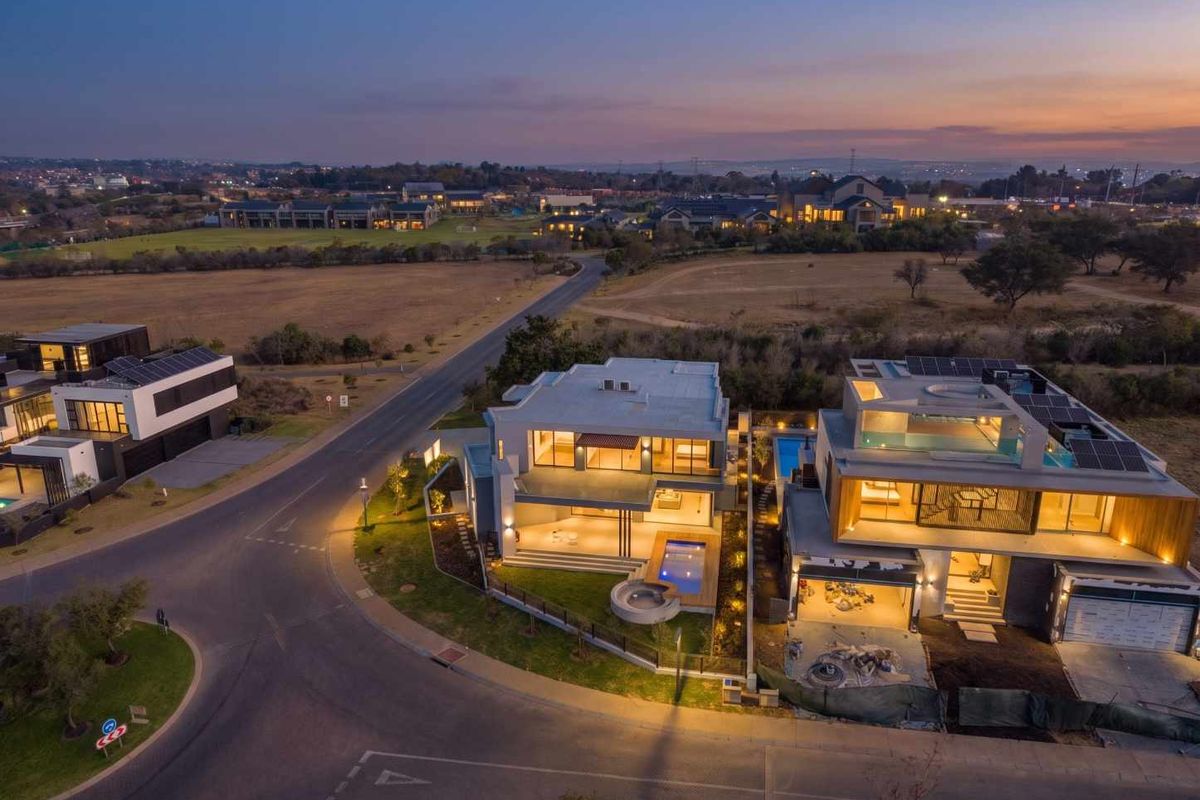 Aerial view of modern residential properties at dusk, featuring swimming pools, solar panels, and landscaped outdoor areas in a suburban estate setting.