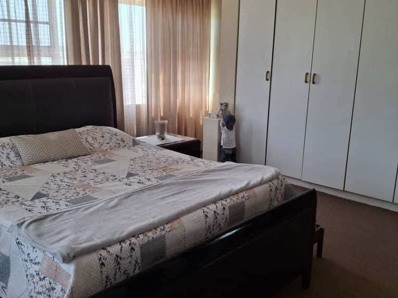 A bedroom featuring wall-to-wall built-in cupboards and large windows with curtains, providing ample storage and natural light.