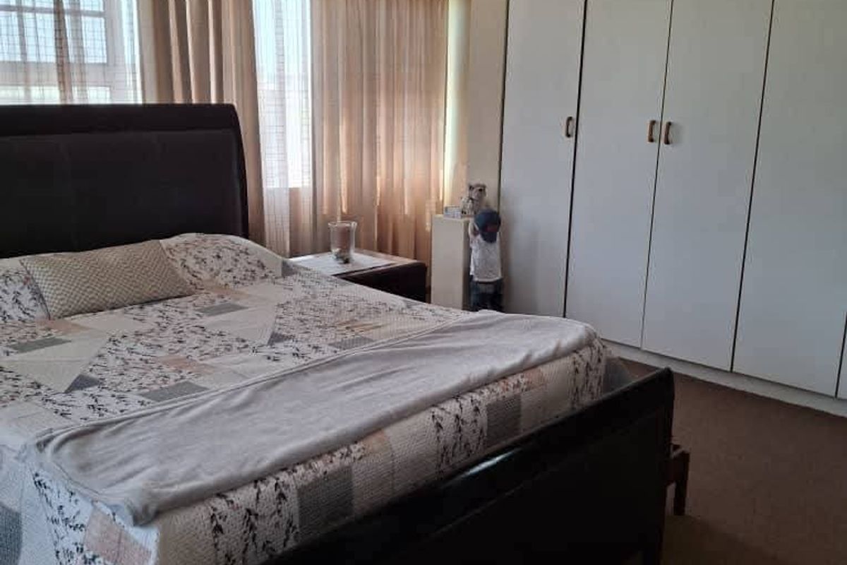 A bedroom featuring wall-to-wall built-in cupboards and large windows with curtains, providing ample storage and natural light.