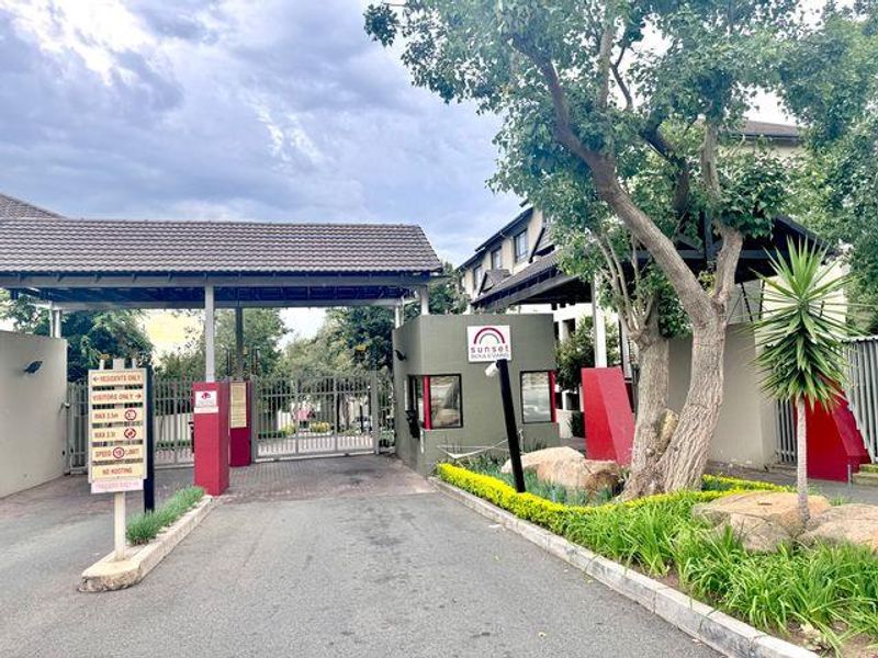 The entrance to Sunset Boulevard apartment complex featuring a secure gated access point, guard house, and paved driveway.