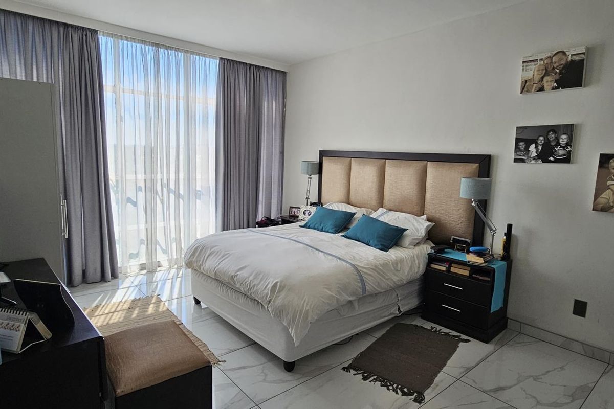 A well-lit bedroom featuring large floor-to-ceiling windows with curtains and modern tiled flooring.