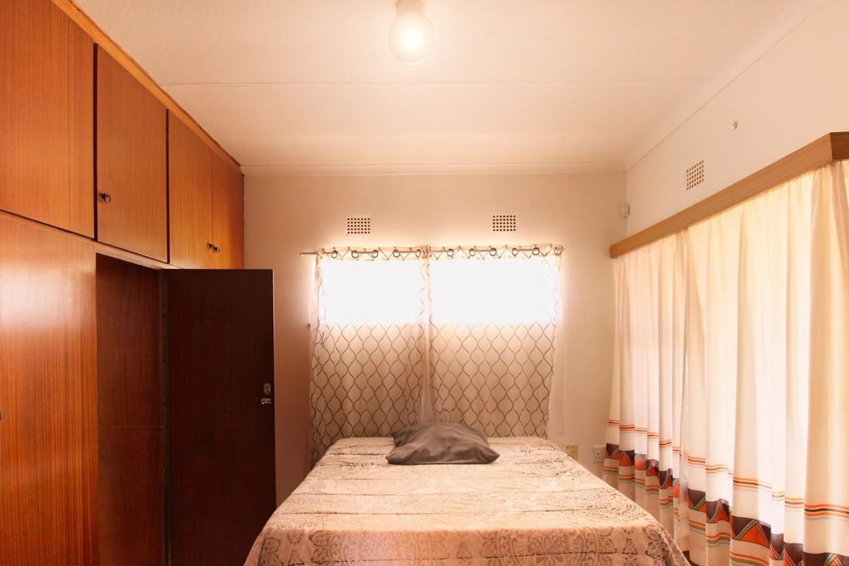 A bedroom featuring extensive built-in wooden cabinetry and natural light through curtained windows.