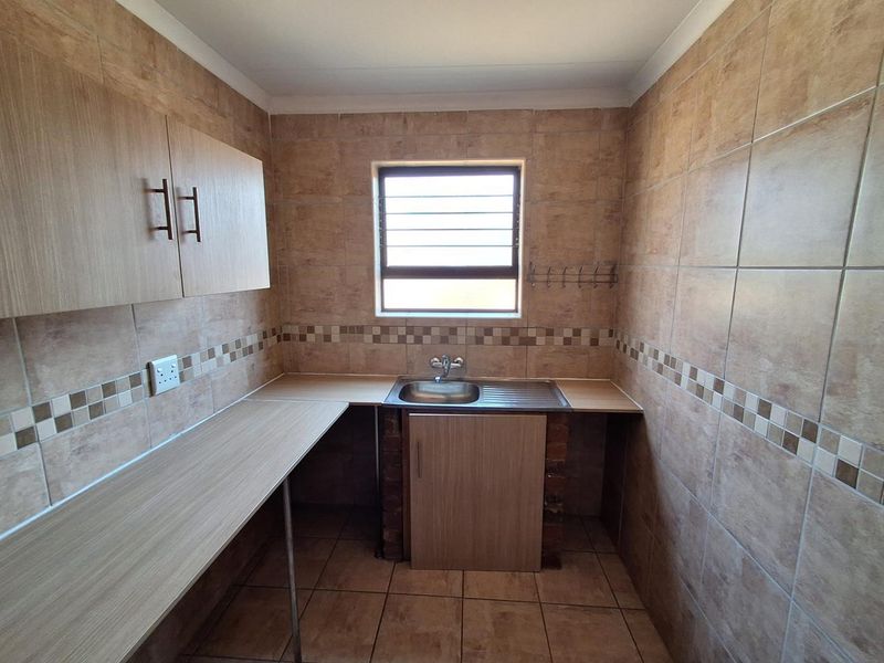 A functional laundry room featuring tiled walls and flooring, built-in cabinetry, and a stainless steel sink with a window for natural light.