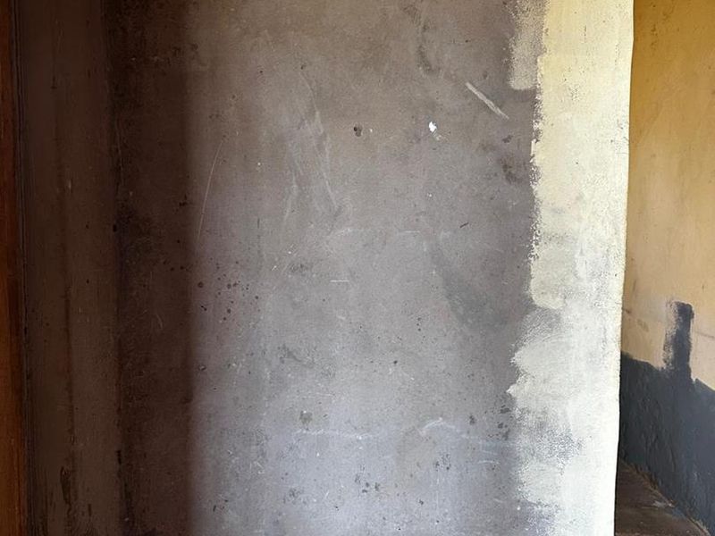 An interior view showing unfinished, raw plaster walls with uneven textures and signs of significant wear and deterioration.