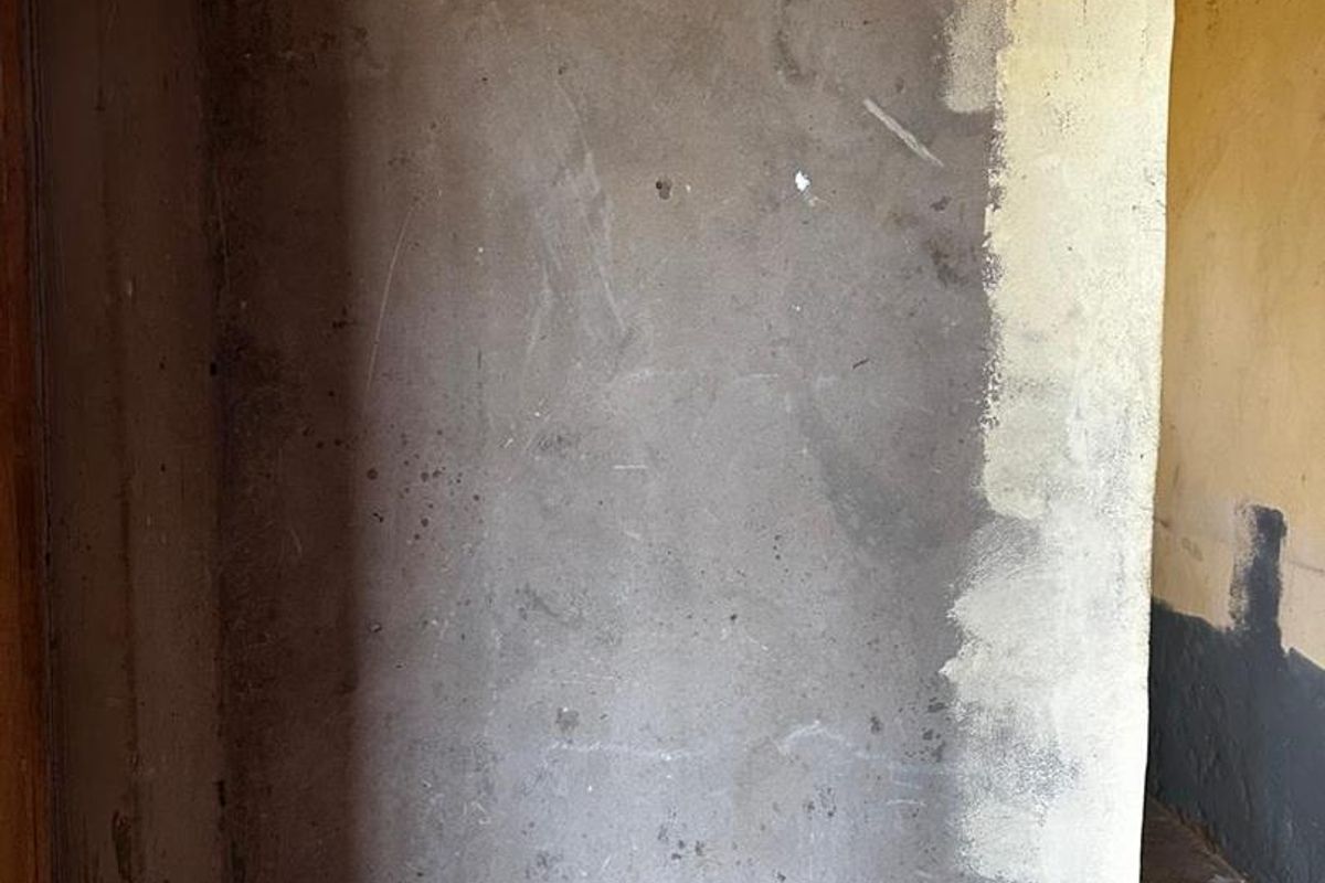An interior view showing unfinished, raw plaster walls with uneven textures and signs of significant wear and deterioration.