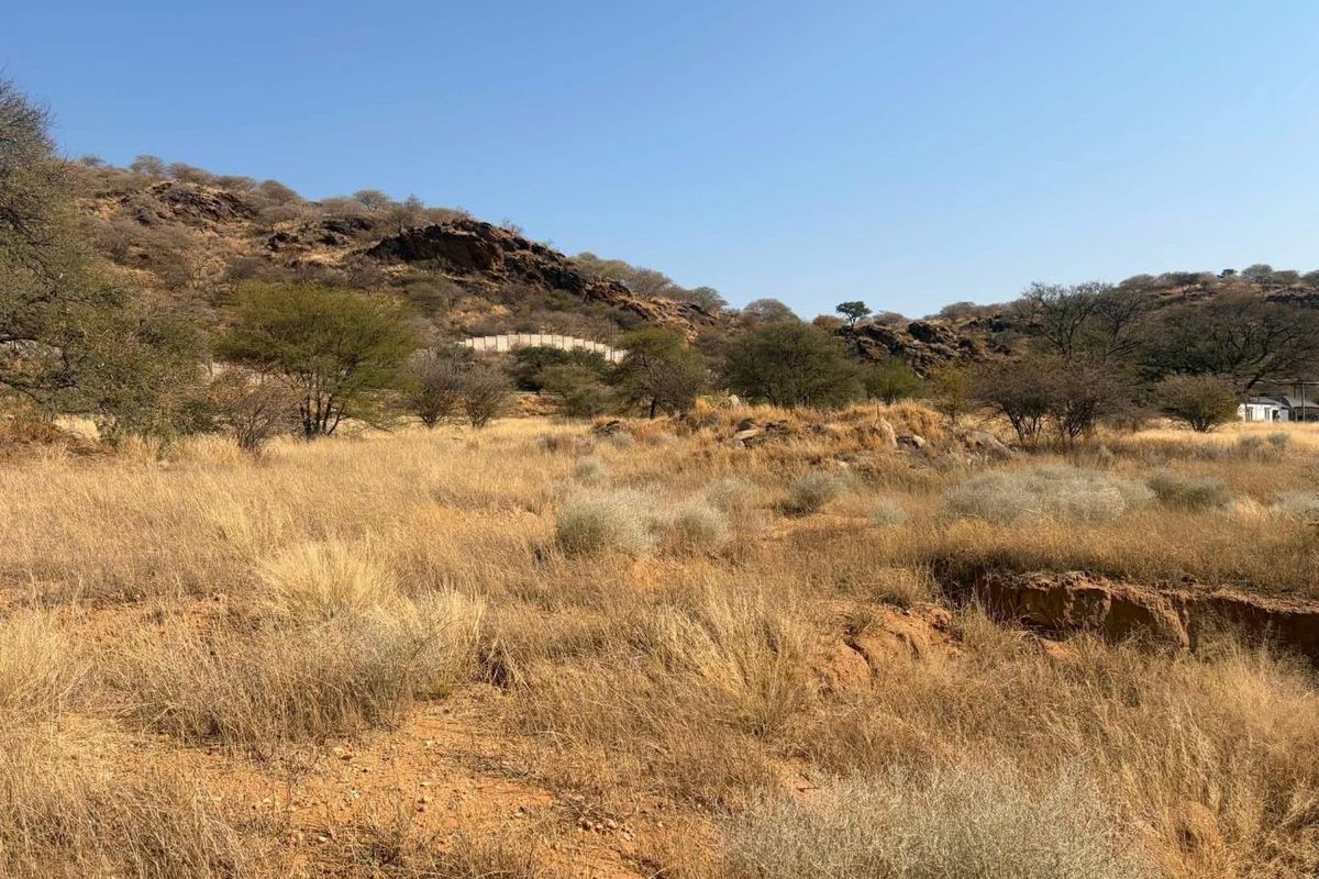 A view of the vacant commercial land featuring natural rocky terrain, indigenous vegetation, and open landscape under a clear sky.