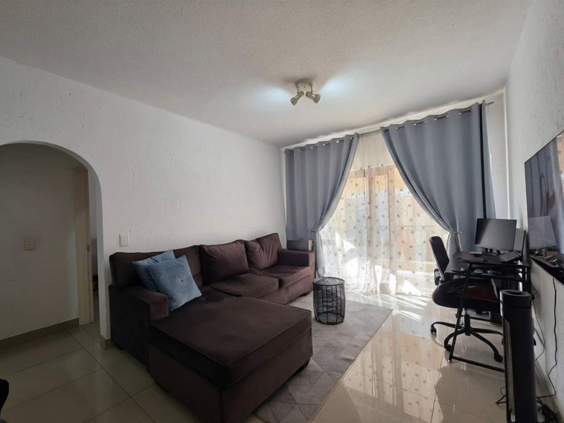 A living room featuring tiled flooring, an arched entryway, and a sliding glass door providing natural light.