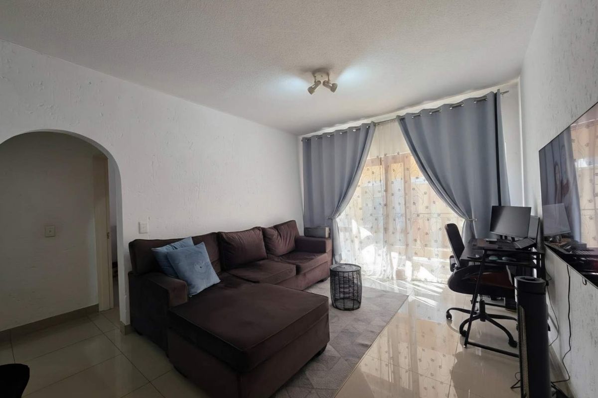 A living room featuring tiled flooring, an arched entryway, and a sliding glass door providing natural light.