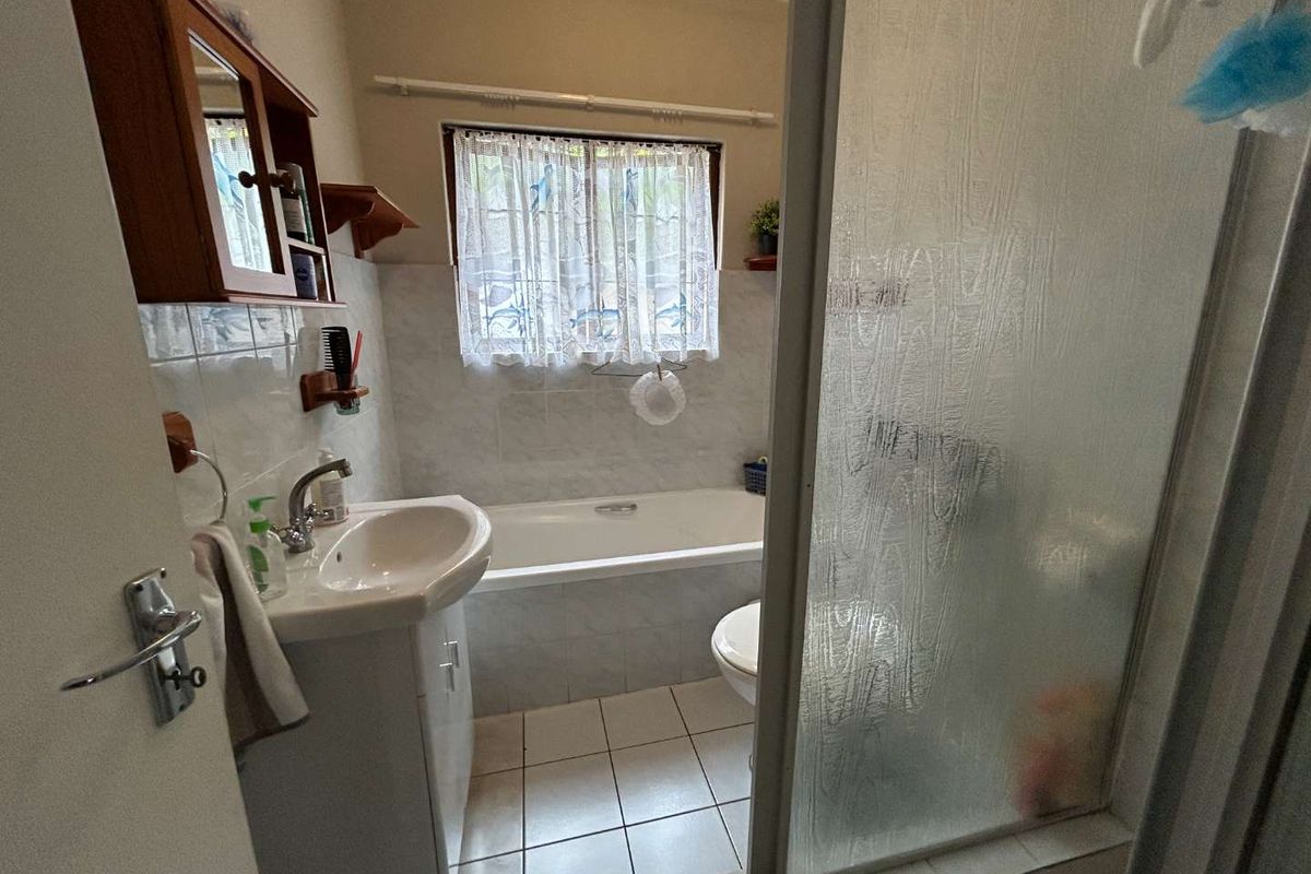 A functional bathroom featuring a built-in bathtub, a separate shower enclosure with textured glass, and a vanity basin with wall-mounted cabinetry.