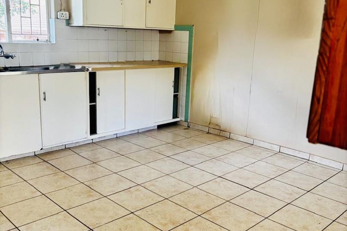 A dated kitchen featuring white cabinetry, tiled flooring, and a stainless steel sink, requiring cosmetic updates and repairs to the flooring and walls.