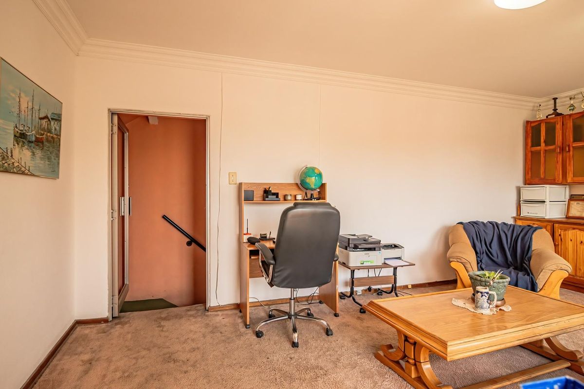 A living area featuring built-in wooden cabinetry, cove cornicing, and direct access to a staircase, with carpeted flooring throughout.