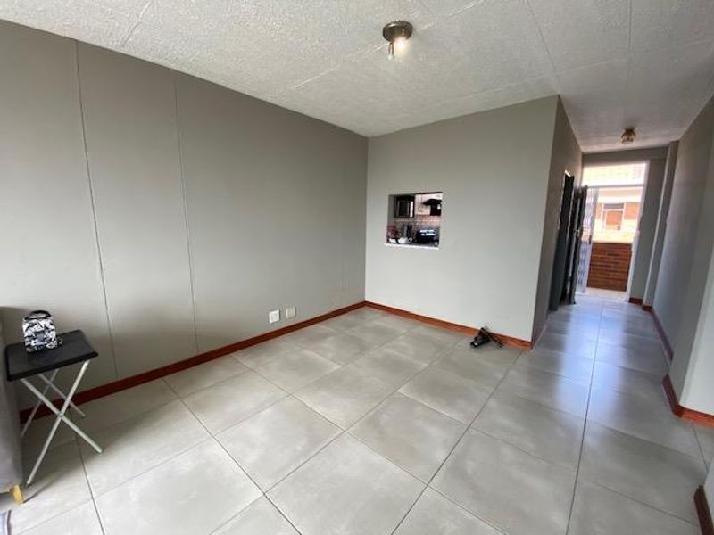 An empty living room featuring large format floor tiles, a pass-through window to the kitchen, and neutral wall tones.
