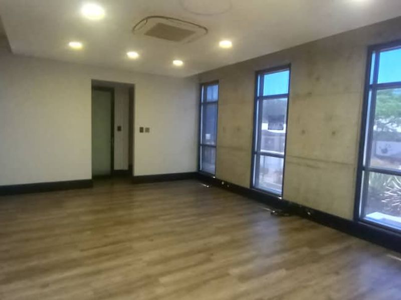A modern, empty office space featuring exposed concrete walls, laminate flooring, large windows, and integrated ceiling lighting and air conditioning.