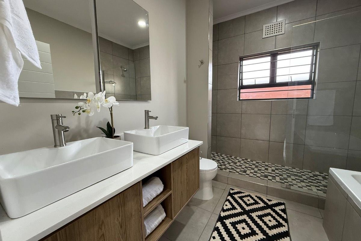 Modern bathroom featuring a double vanity with vessel sinks, wood-finish cabinetry, and a spacious walk-in shower with tiled flooring.
