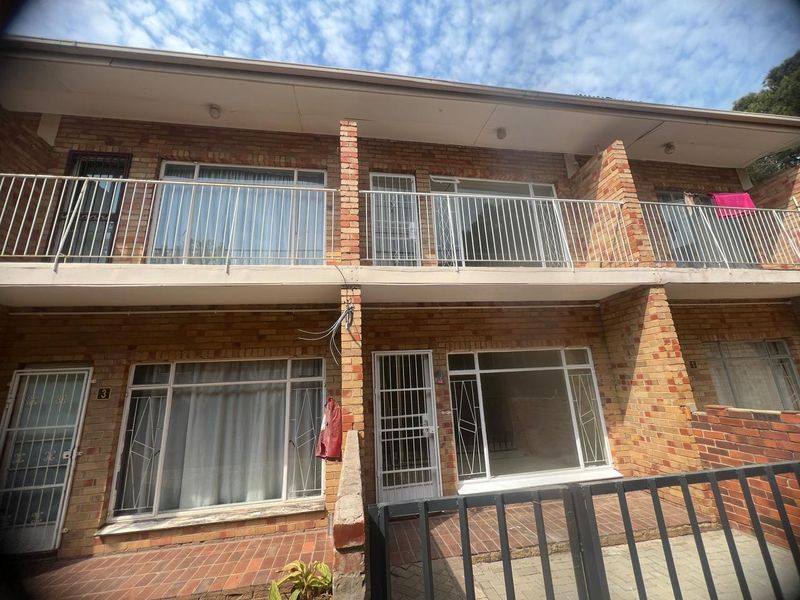 Front elevation of a two-story apartment complex featuring face brick construction, metal security gates, and upper-level balconies with metal railings.