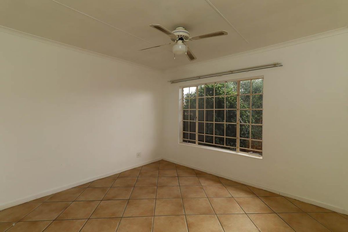 A bright, empty bedroom featuring neutral tiled flooring, a ceiling fan, and a large grid-pattern window overlooking the garden.