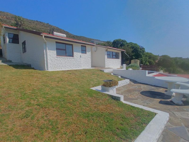 Rear view of the property featuring a stone-paved patio, landscaped lawn, and white exterior walls with a tiled roof.