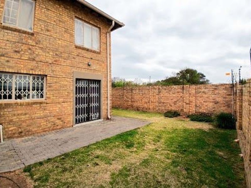 Rear view of a townhouse featuring a brick facade, paved patio area, and a private garden enclosed by brick boundary walls with electric fencing.
