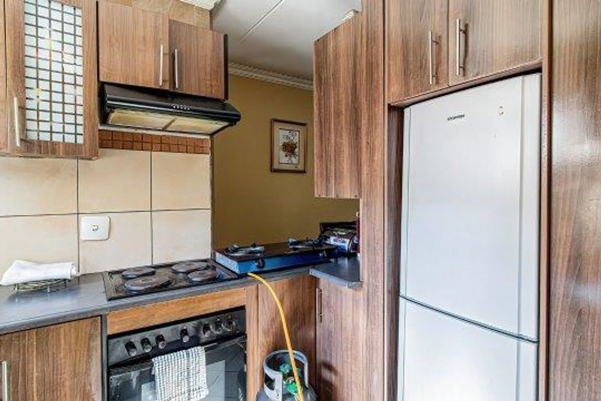 Compact kitchen featuring wood-look cabinetry, built-in oven, electric hob, extractor fan, and tiled backsplash, offering functional storage and preparation space.