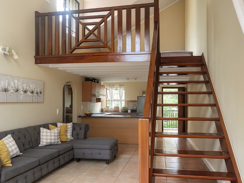 Open plan living area featuring a wooden staircase leading to a mezzanine level, tiled floors, and an integrated kitchen with wooden cabinetry.