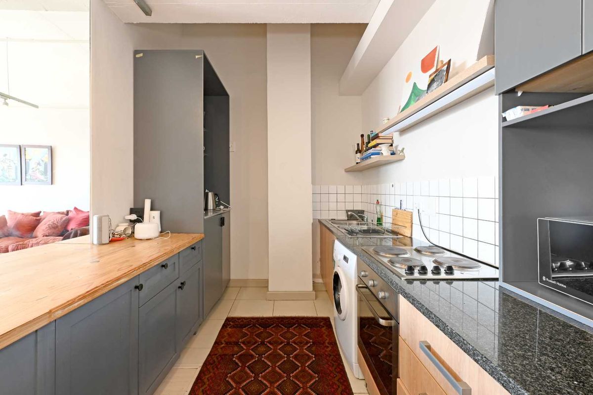 A functional galley-style kitchen featuring dark grey cabinetry, stone countertops, a built-in oven, electric hob, and integrated laundry appliance space.