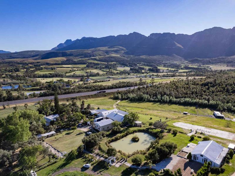 Aerial view of a farm property featuring multiple buildings, a dam, and expansive mountain views in a rural landscape.
