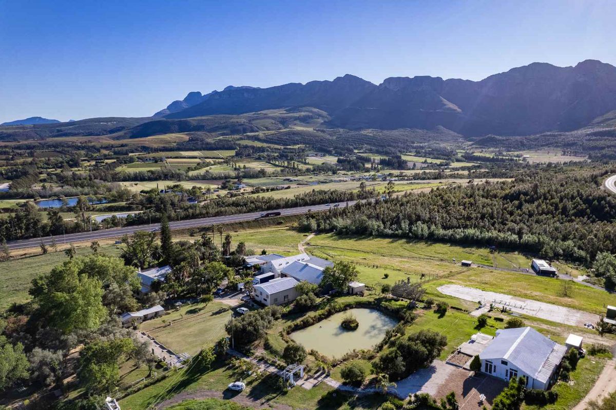 Aerial view of a farm property featuring multiple buildings, a dam, and expansive mountain views in a rural landscape.