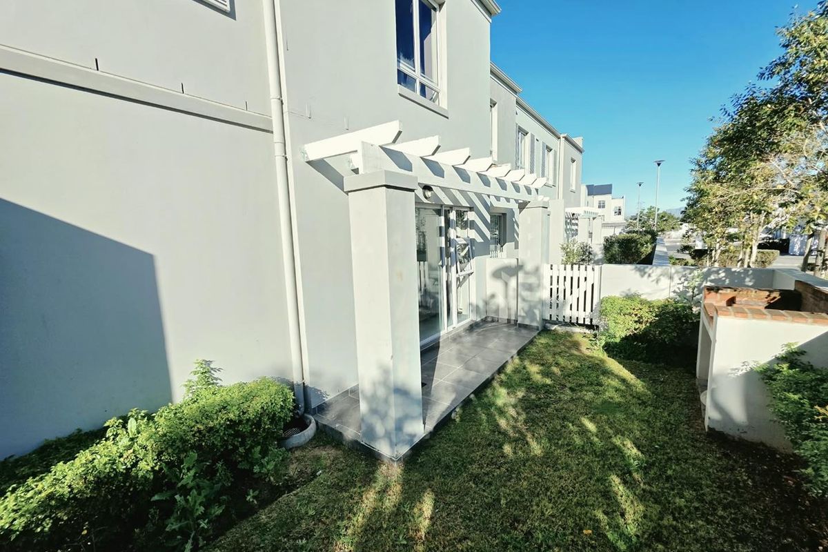 Rear exterior view featuring a paved patio with a pergola, a built-in braai, and a small private garden area.