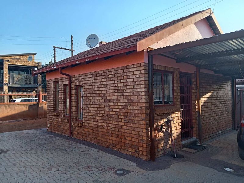 A single-story face brick house featuring a tiled roof, a covered carport, and secure metal entrance gate, situated on a paved driveway.