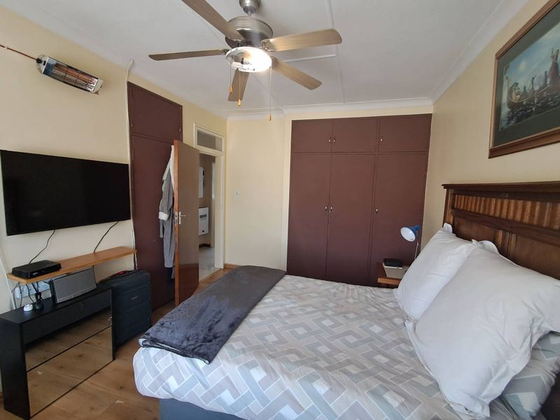 A functional bedroom featuring built-in cupboards, a ceiling fan, and laminate flooring, providing a comfortable and practical living space.
