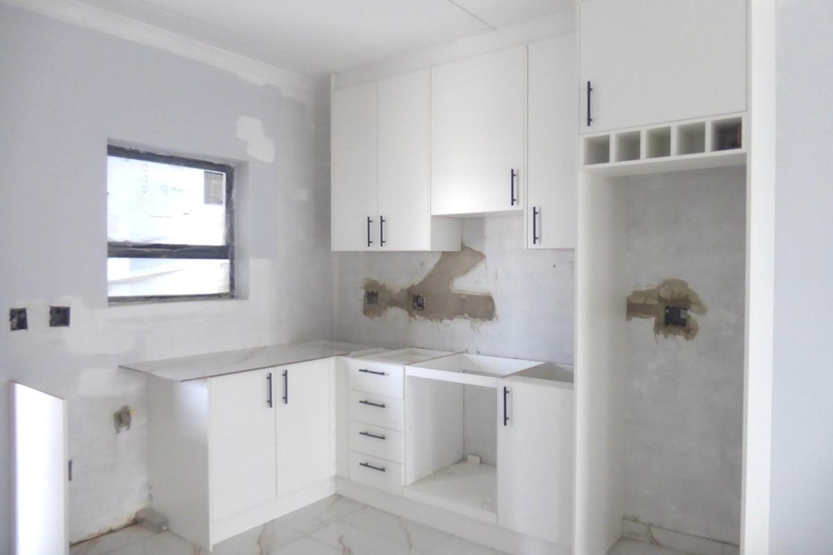 An unfinished kitchen space featuring white cabinetry, marble-look floor tiles, and a wine rack, currently requiring wall finishing and final appliance installation.
