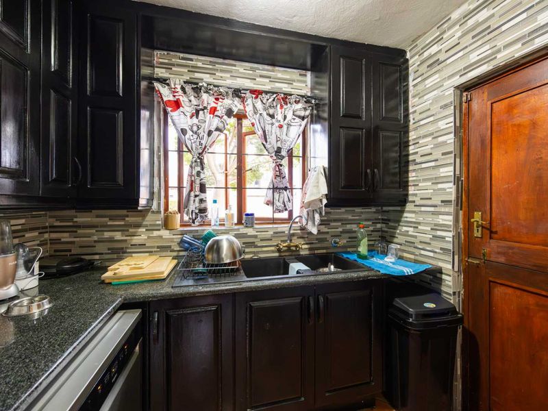 A compact kitchen featuring dark cabinetry, granite countertops, a double basin sink, and a decorative tiled backsplash.