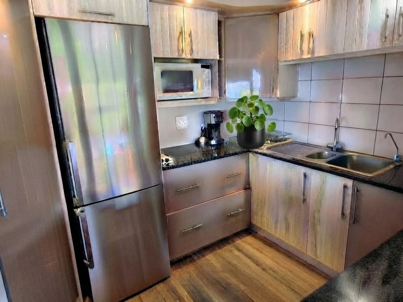 A functional kitchen featuring wood-finish cabinetry, granite countertops, a stainless steel sink, and a built-in microwave with a tiled backsplash.