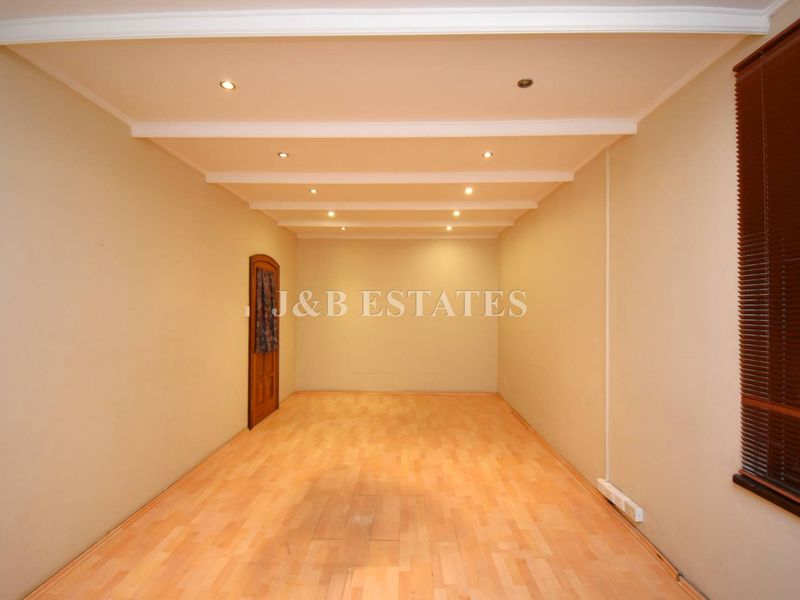 An empty, versatile retail space featuring recessed ceiling lighting, wood-look laminate flooring, and a single wooden door.