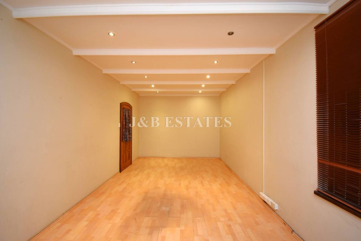 An empty, versatile retail space featuring recessed ceiling lighting, wood-look laminate flooring, and a single wooden door.