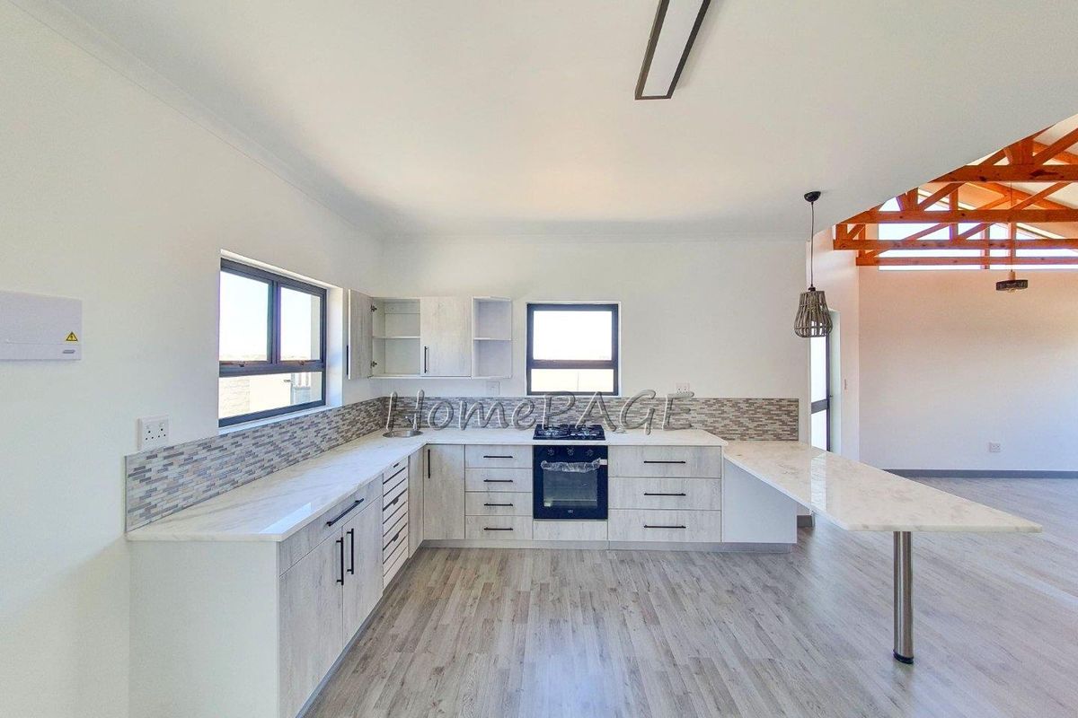 Modern open-plan kitchen featuring light wood-grain cabinetry, stone countertops, a built-in oven, gas hob, and a breakfast bar extension.