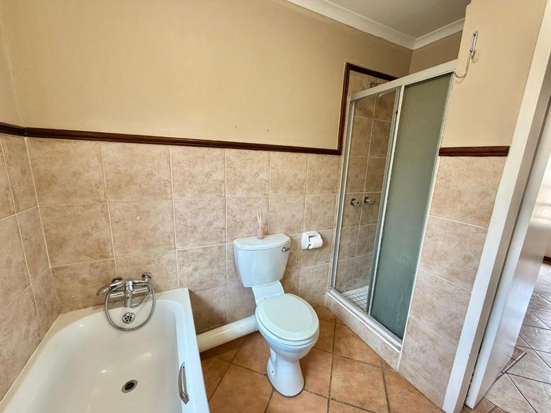 A functional bathroom featuring a bathtub, separate shower enclosure, and toilet, finished with neutral ceramic wall and floor tiles.